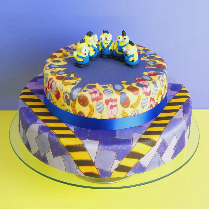 Minions® auf zweistöckiger schurkischer Muster-Torte